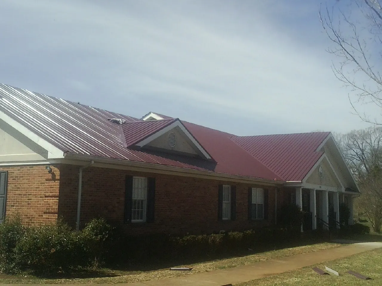 Red metal roof with gabled entries on a long brick building, from a Hail Damage Roof Repair job in Selah