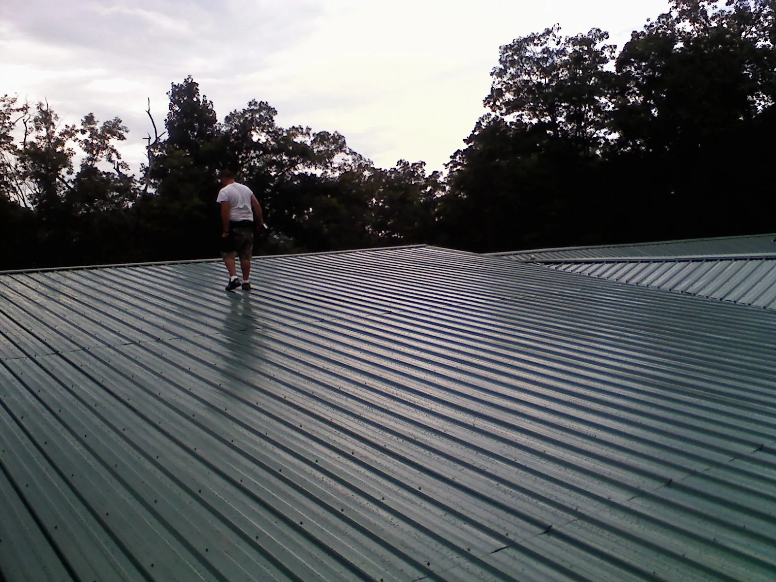 Roofer walking a wide expanse of new green metal roofing in Selah