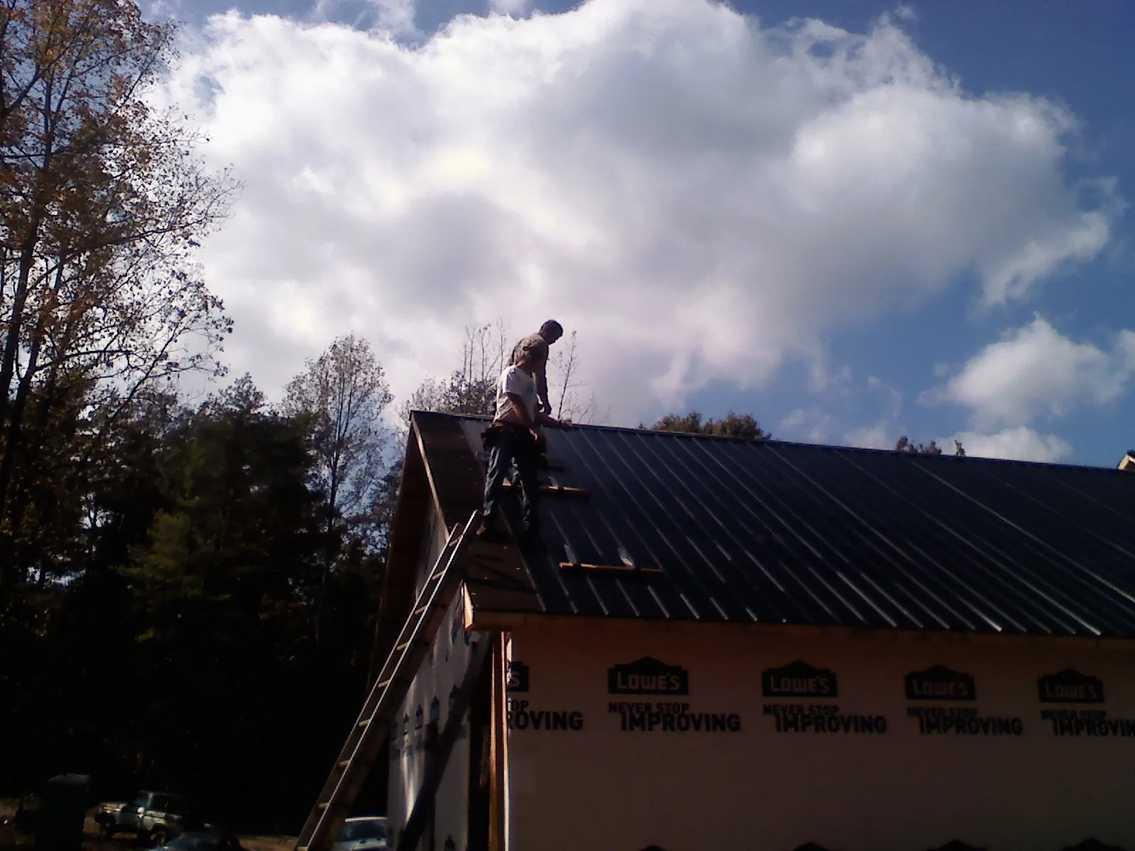 Roofer fastening dark metal panels high against a cloudy sky, from a Roof Inspection job in Selah